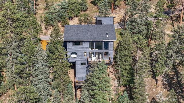 Gray multi-story house nestled among pine trees on a wooded hillside.