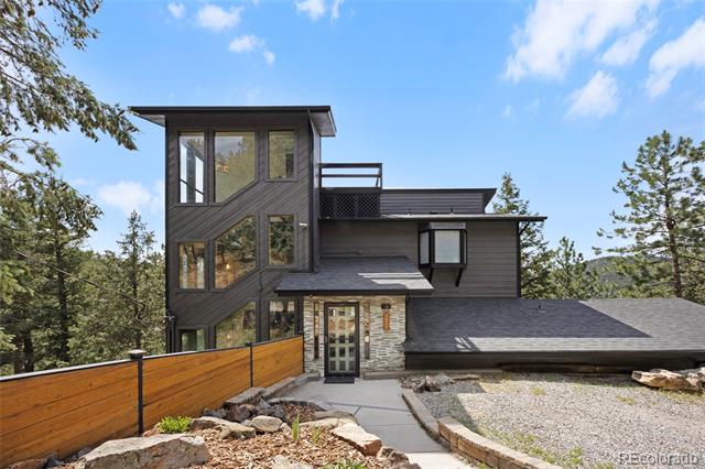 Modern multi-story home with dark siding, tall windows, stone entry, and wood fence.
