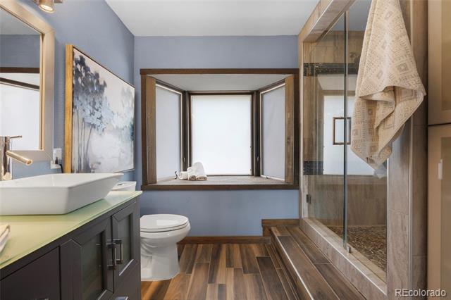 Bathroom with a vessel sink, dark vanity, wood-look floor, and glass-enclosed shower.