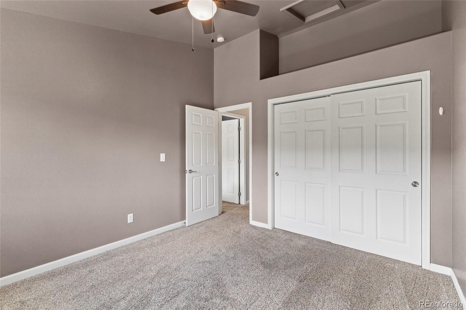 Empty bedroom with gray carpet, a ceiling fan, and white closet doors.