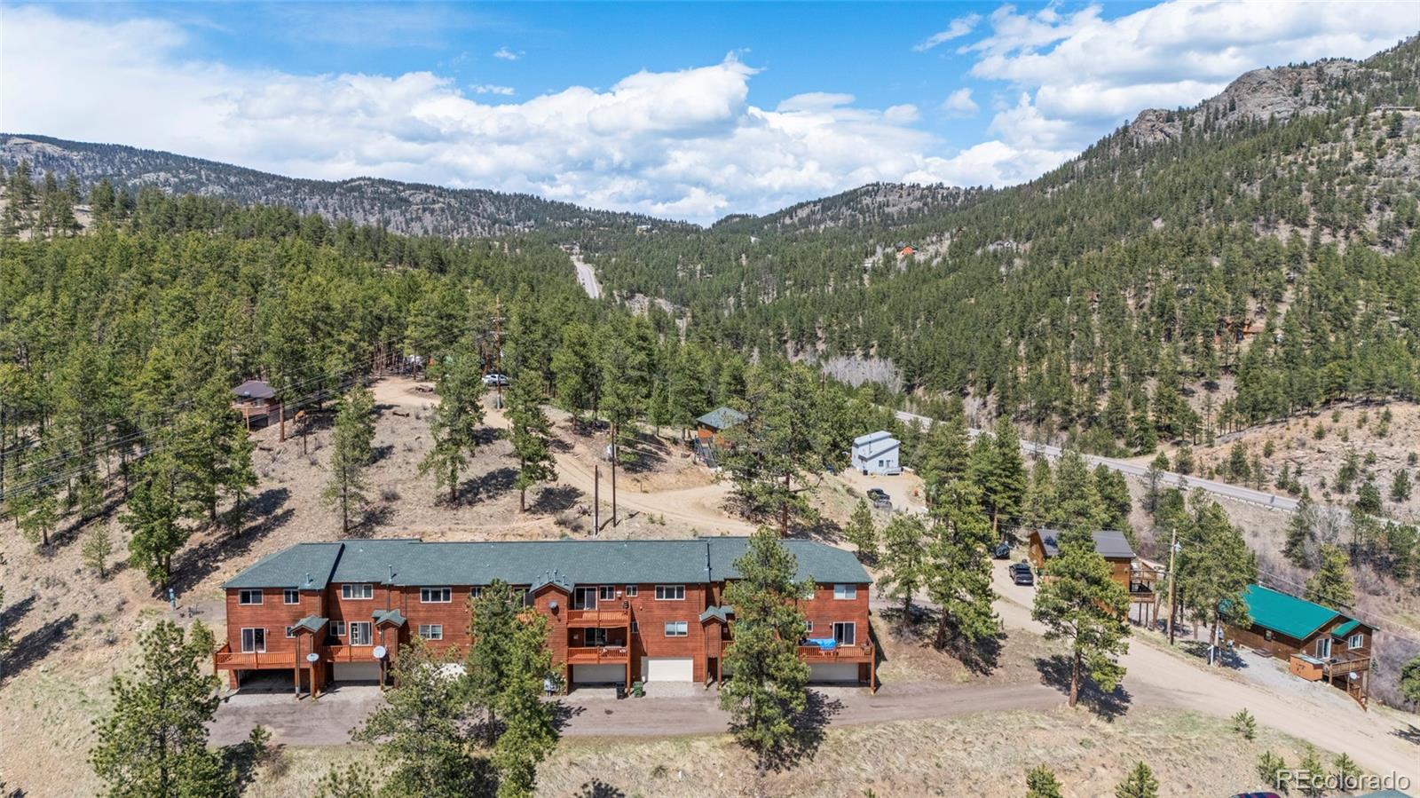 Aerial view of a red multi-unit building amid pine-covered mountain slopes.