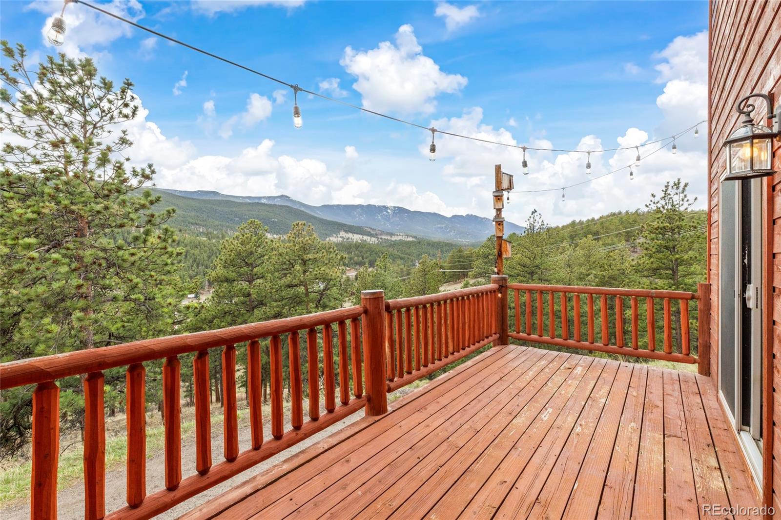 Wooden deck with string lights overlooking pine-covered mountains and a forested valley.