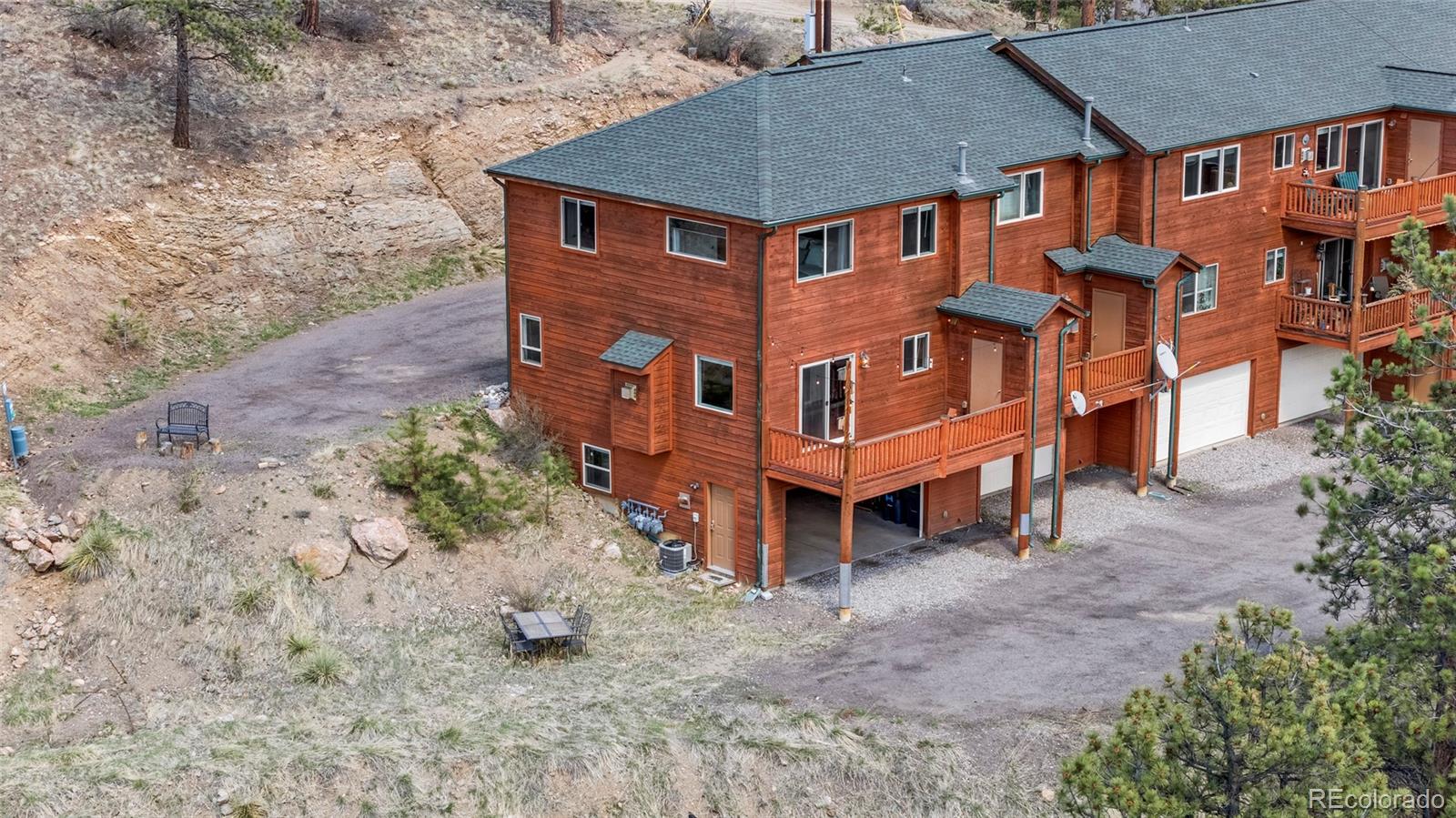 Wood-sided multi-unit residence with balconies and garage bays beside a rocky hillside.