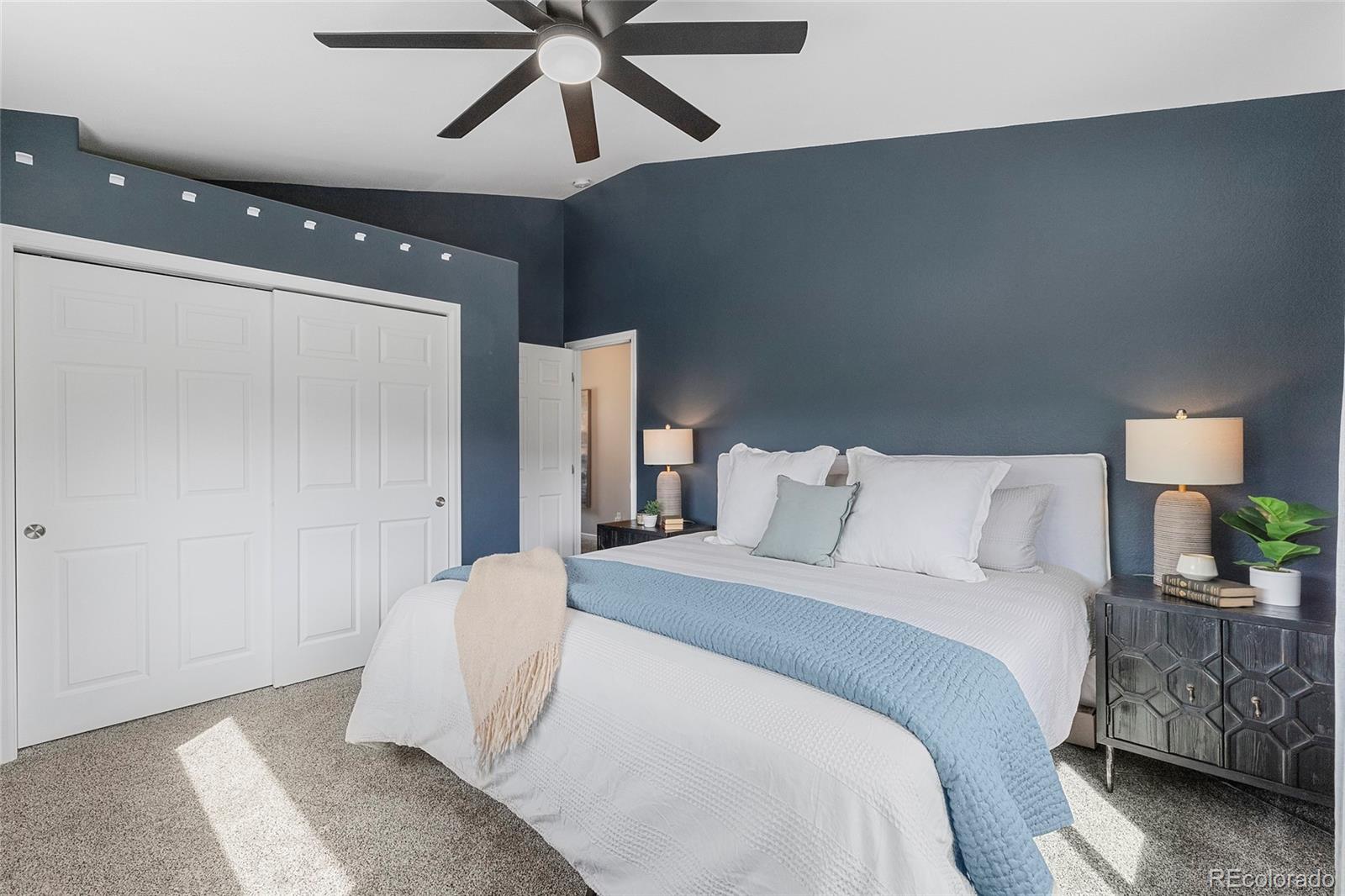 Staged bedroom with a white bed, pale blue coverlet, dark blue walls, and ceiling fan.