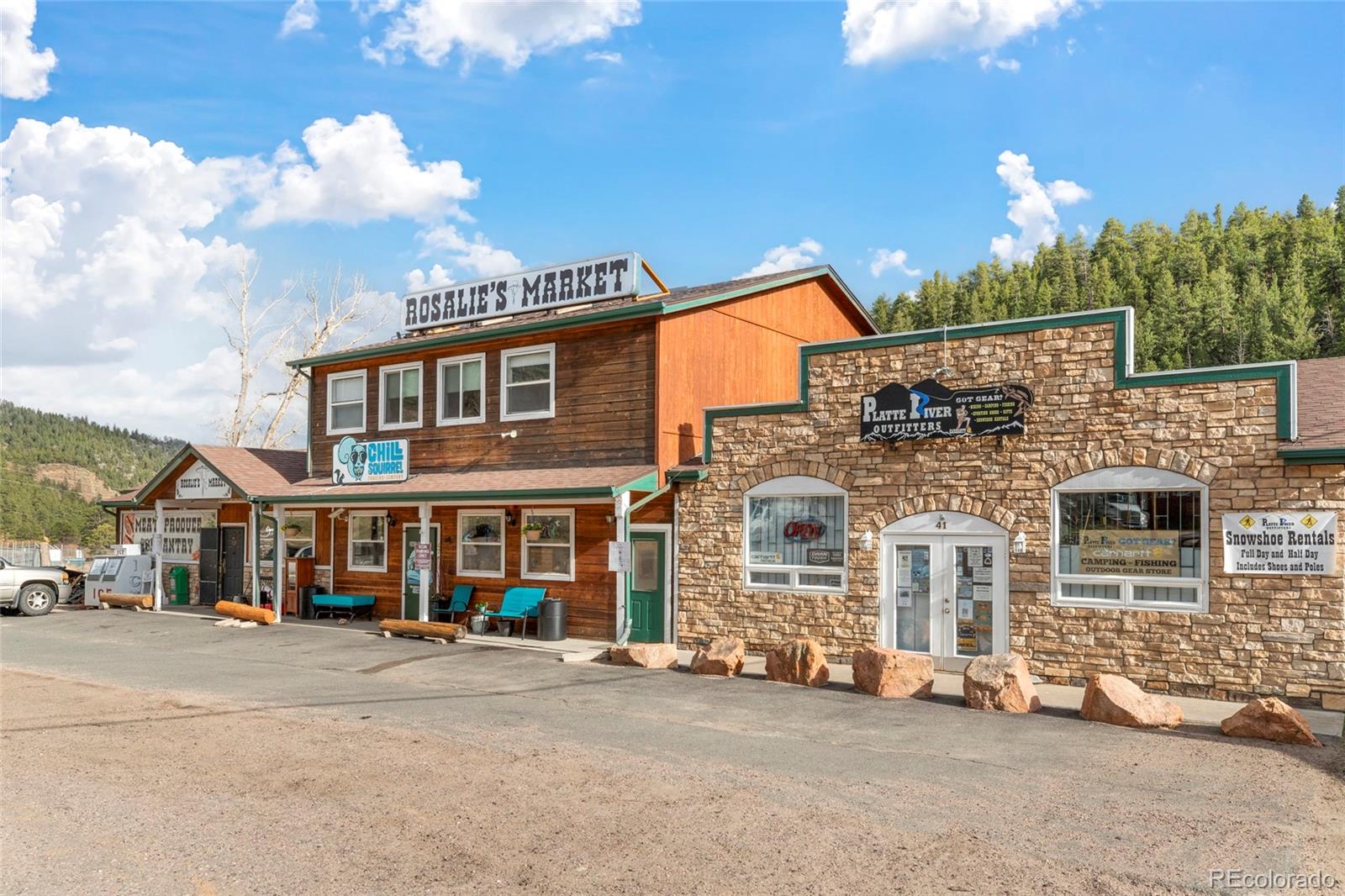 Rustic storefront with Rosalie’s Market and Platte River Outfitters signs, backed by wooded hills.