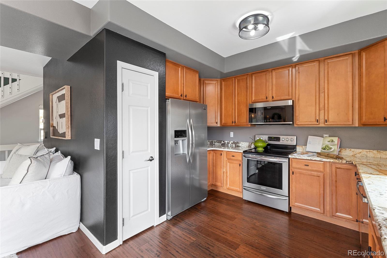Kitchen with honey-colored cabinets, granite counters, stainless steel appliances, and dark hardwood floors.
