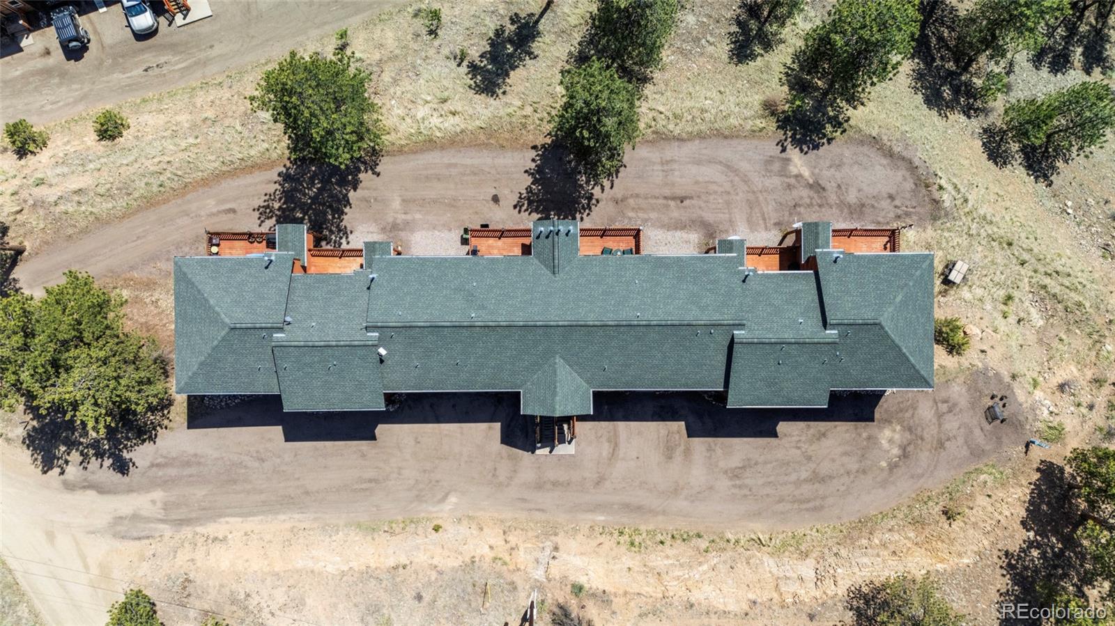 Aerial view of a long residential building with green roof, patios, and surrounding dirt drive.