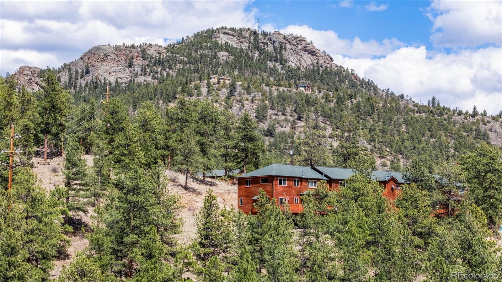 Mountain-side residence among pine trees below a rocky ridge.