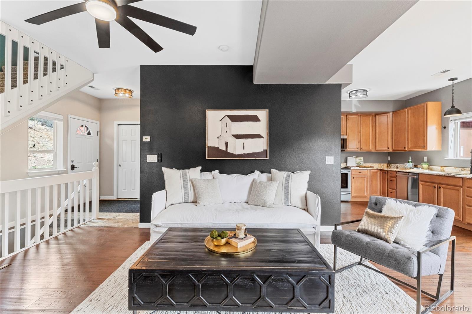 Living room with white sofa against a charcoal wall, dark coffee table, and open kitchen with wood cabinets.