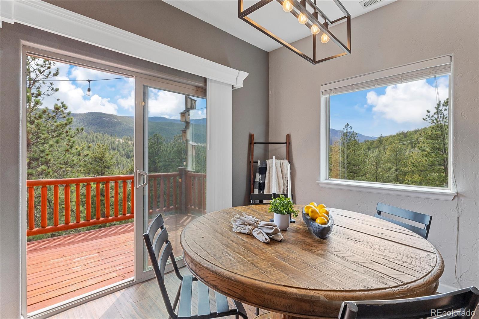 Dining area with a round wooden table, deck access, and forested mountain views.