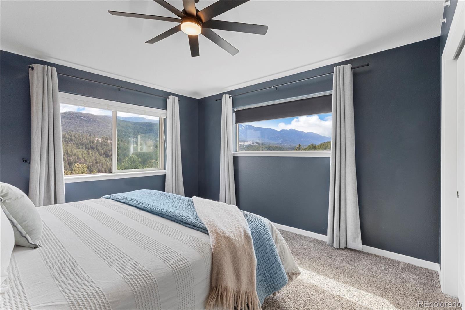 Bedroom with dark blue walls, a white bed, and mountain views through two windows.