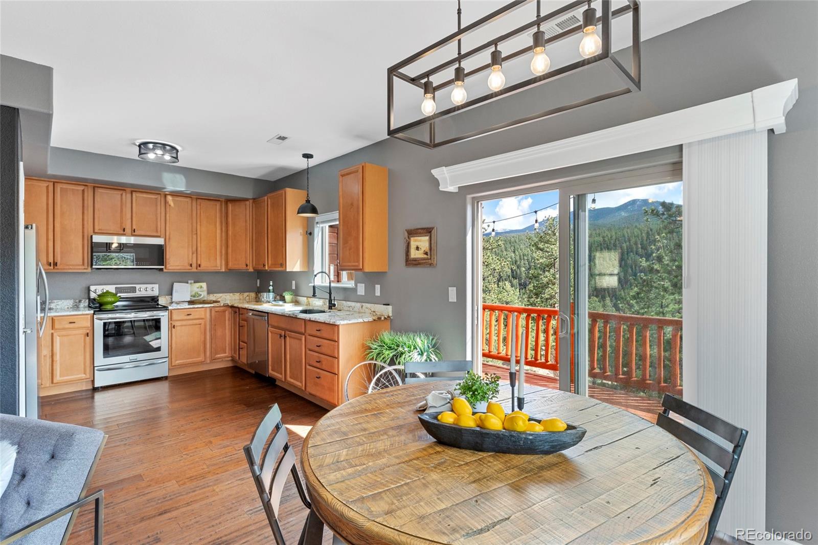 Kitchen and dining area with wood cabinets, a round table, and forested mountain views through sliding glass doors.