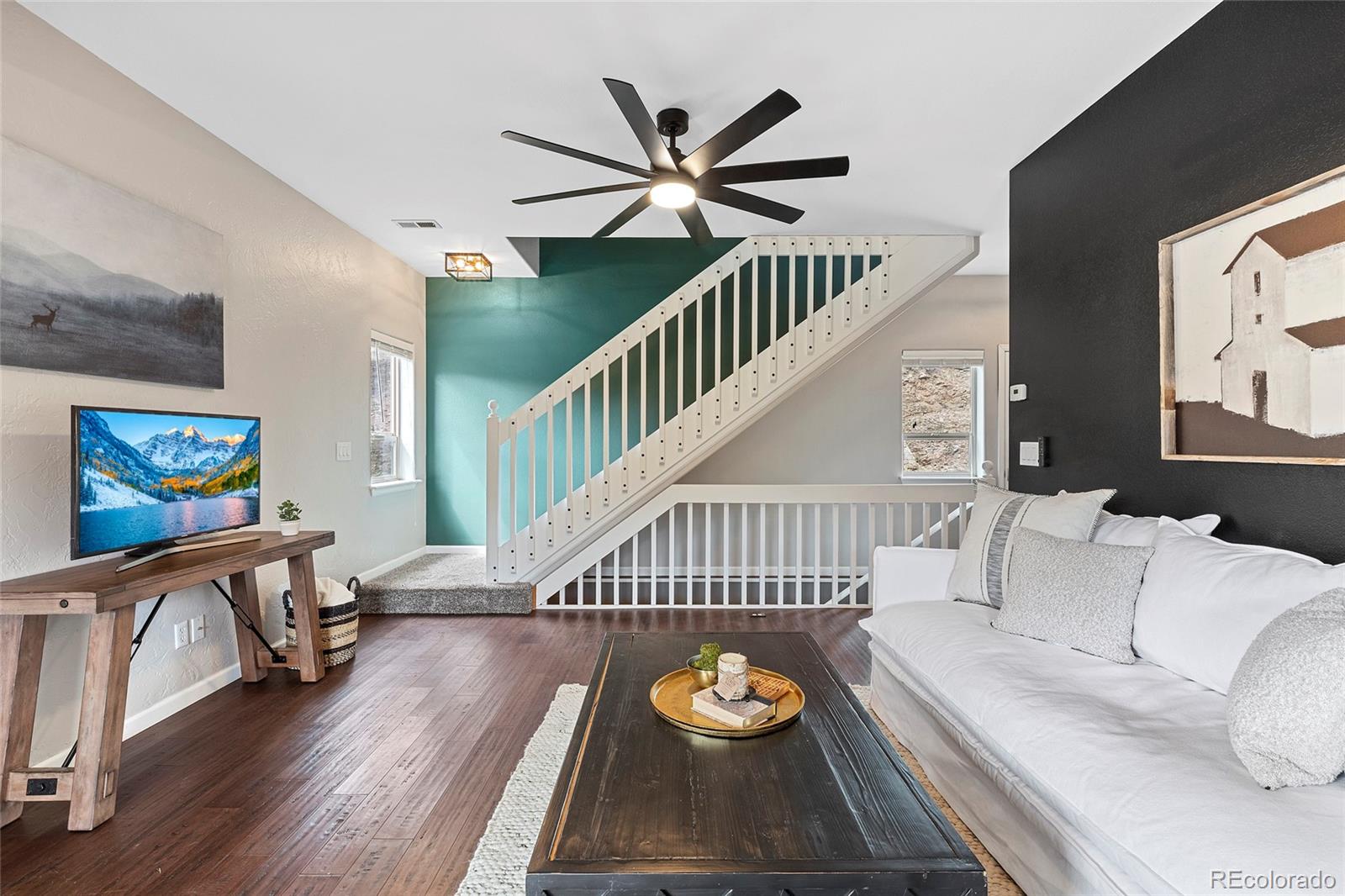 Living room with a white sofa and coffee table beside a staircase against a teal accent wall.