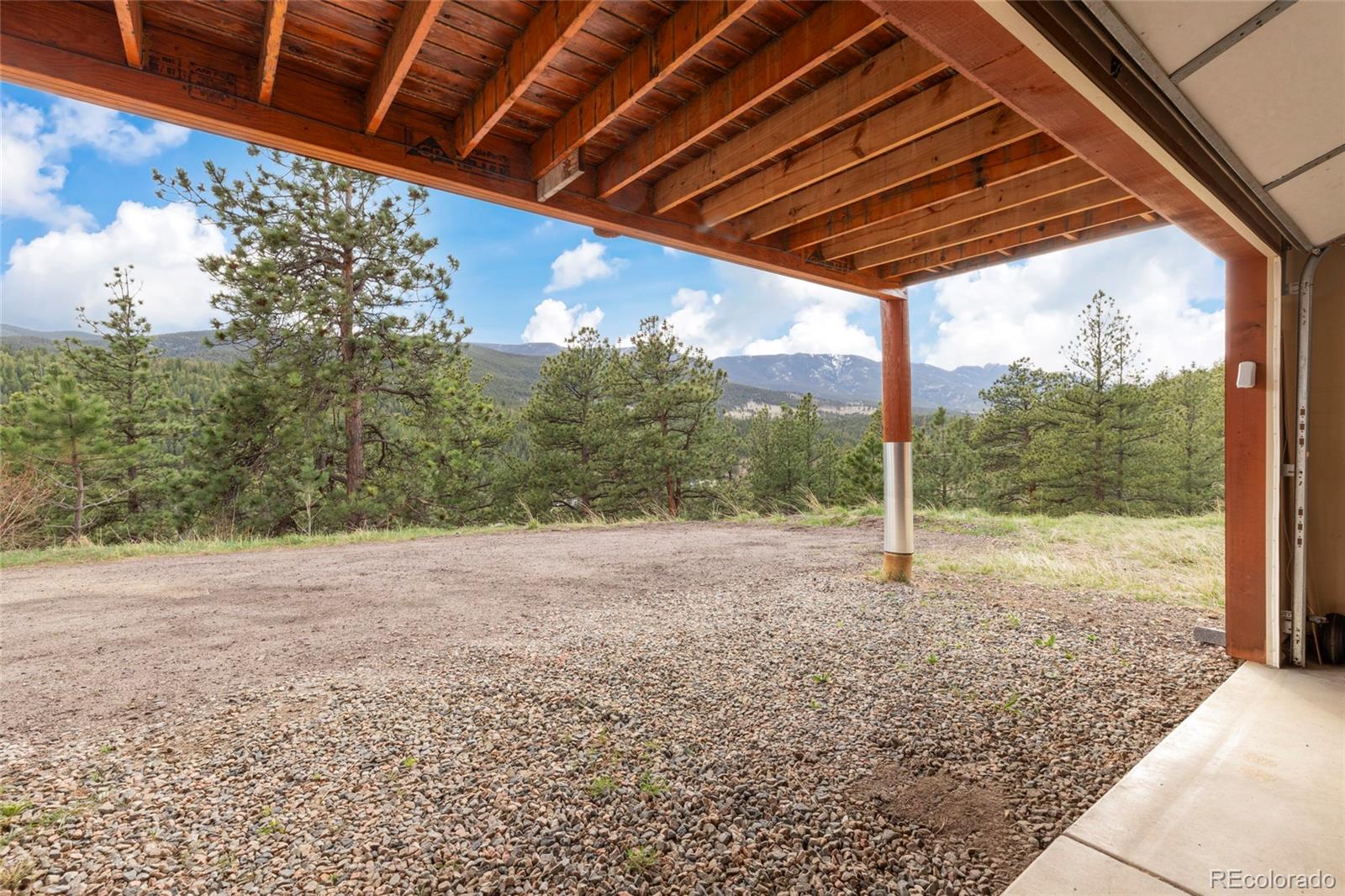 Covered gravel parking area opens to pine-covered hills and distant mountain views.