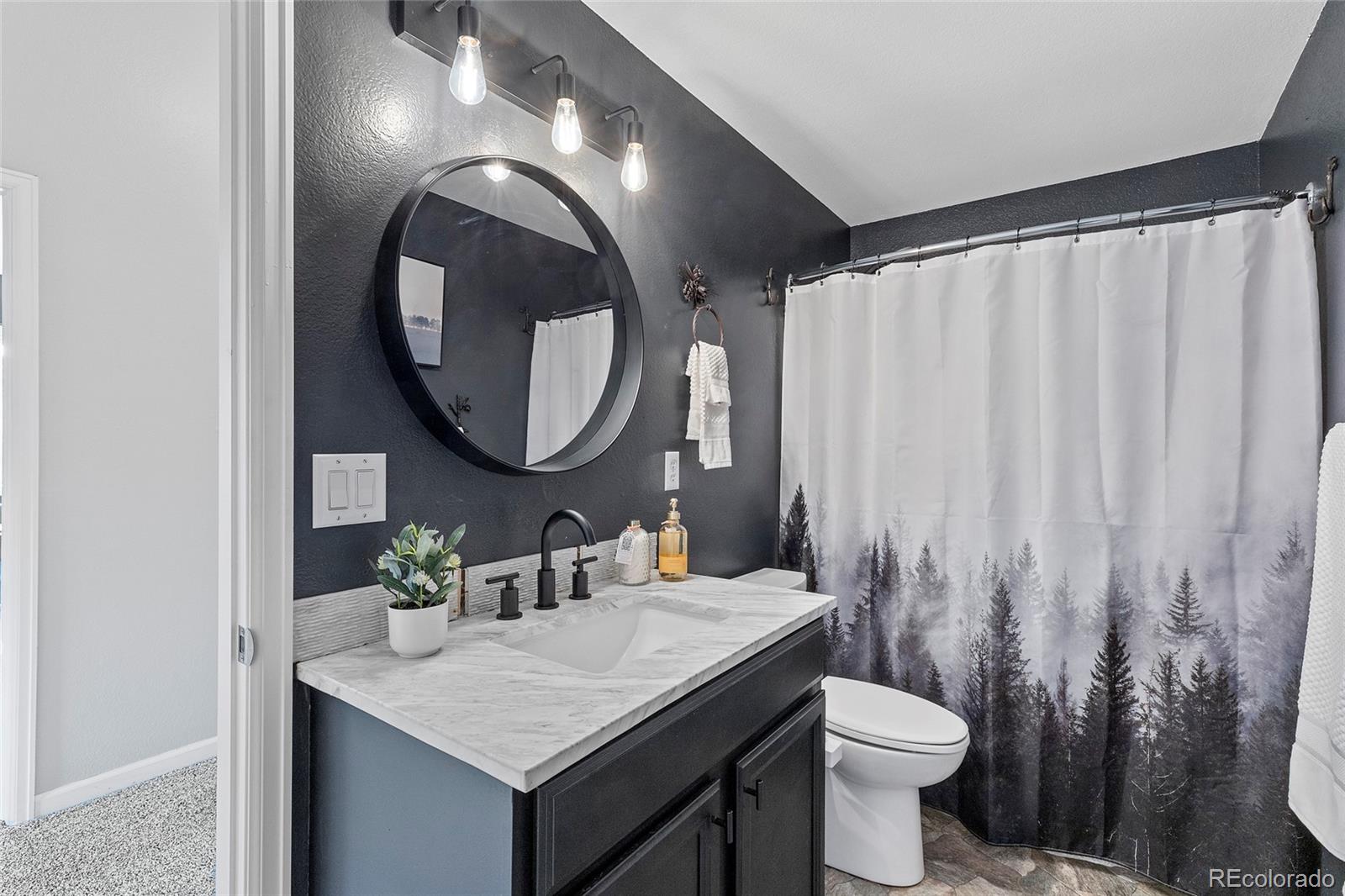 Bathroom with a marble-look vanity, round mirror, and forest-print shower curtain.