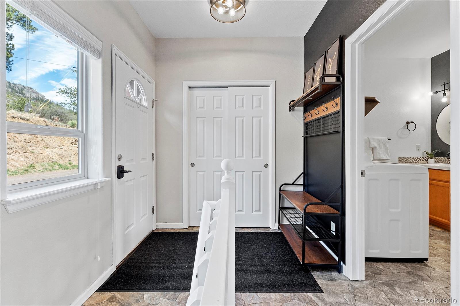 Entry foyer with a window overlooking a rocky hillside, bench and coat rack, and adjoining bathroom.
