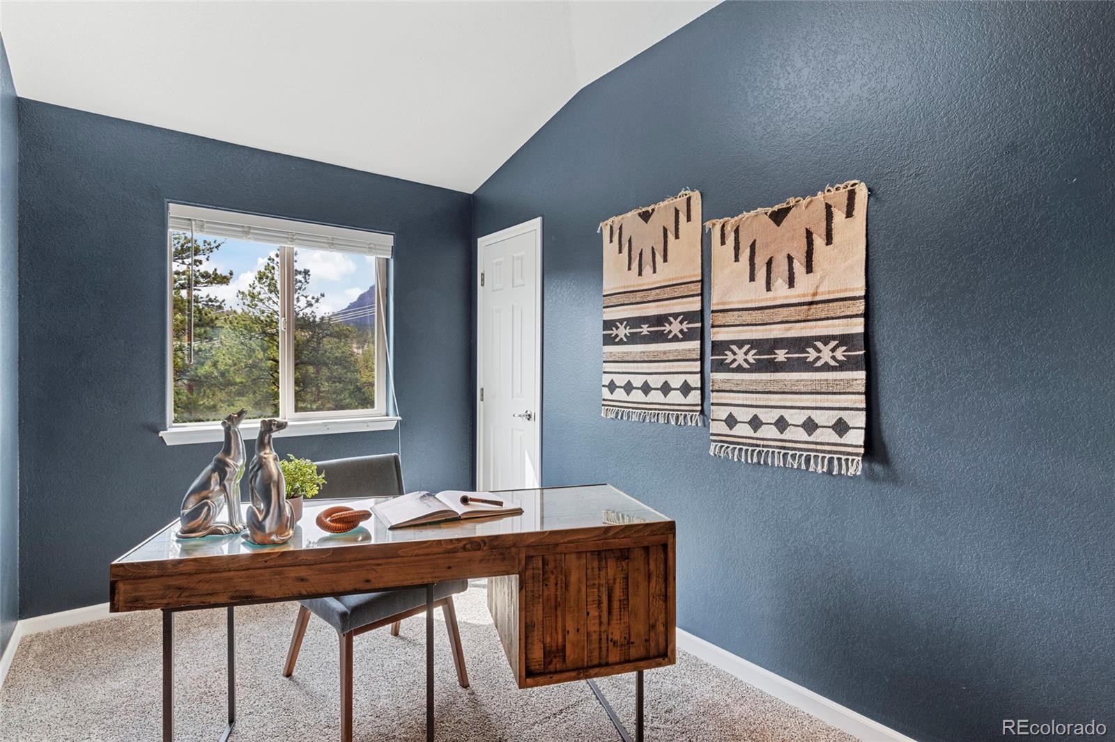 Staged home office with a glass-top wooden desk and a window overlooking trees and a mountain.