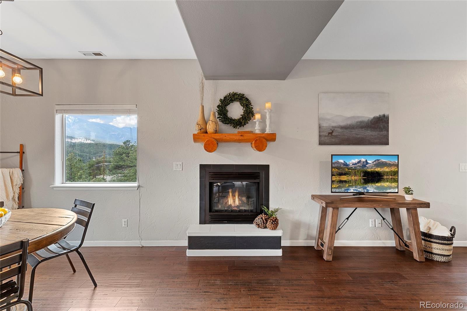 Living room with a lit fireplace, rustic mantel, and mountain view through the window.