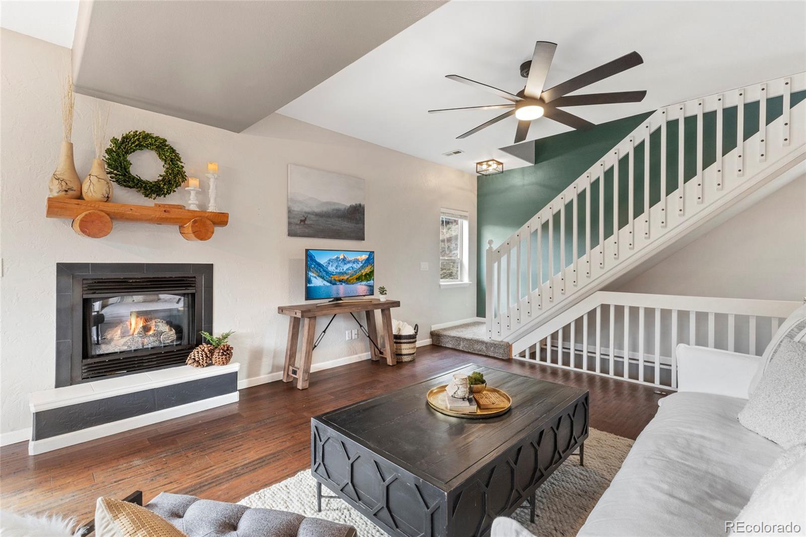 Living room with a fireplace, dark wood floors, and a staircase with white railing.