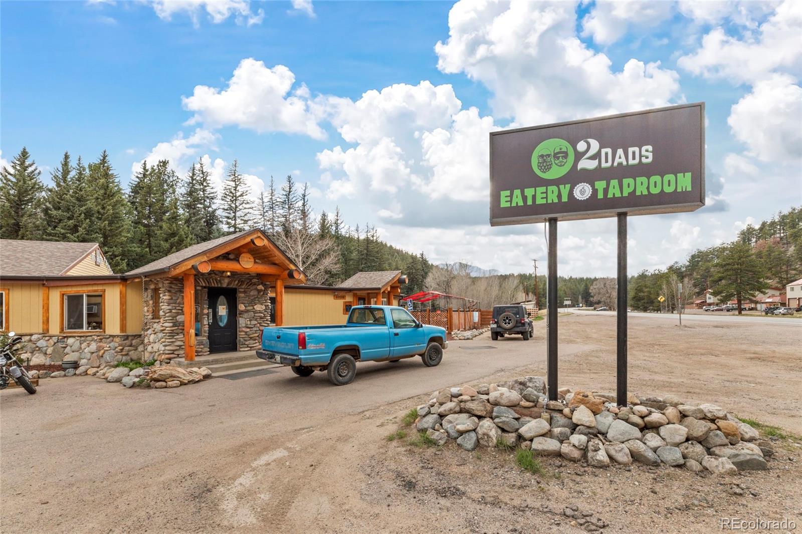 Rustic stone-and-wood eatery beneath a 2 Dads Eatery Taproom sign, with trucks parked outside.