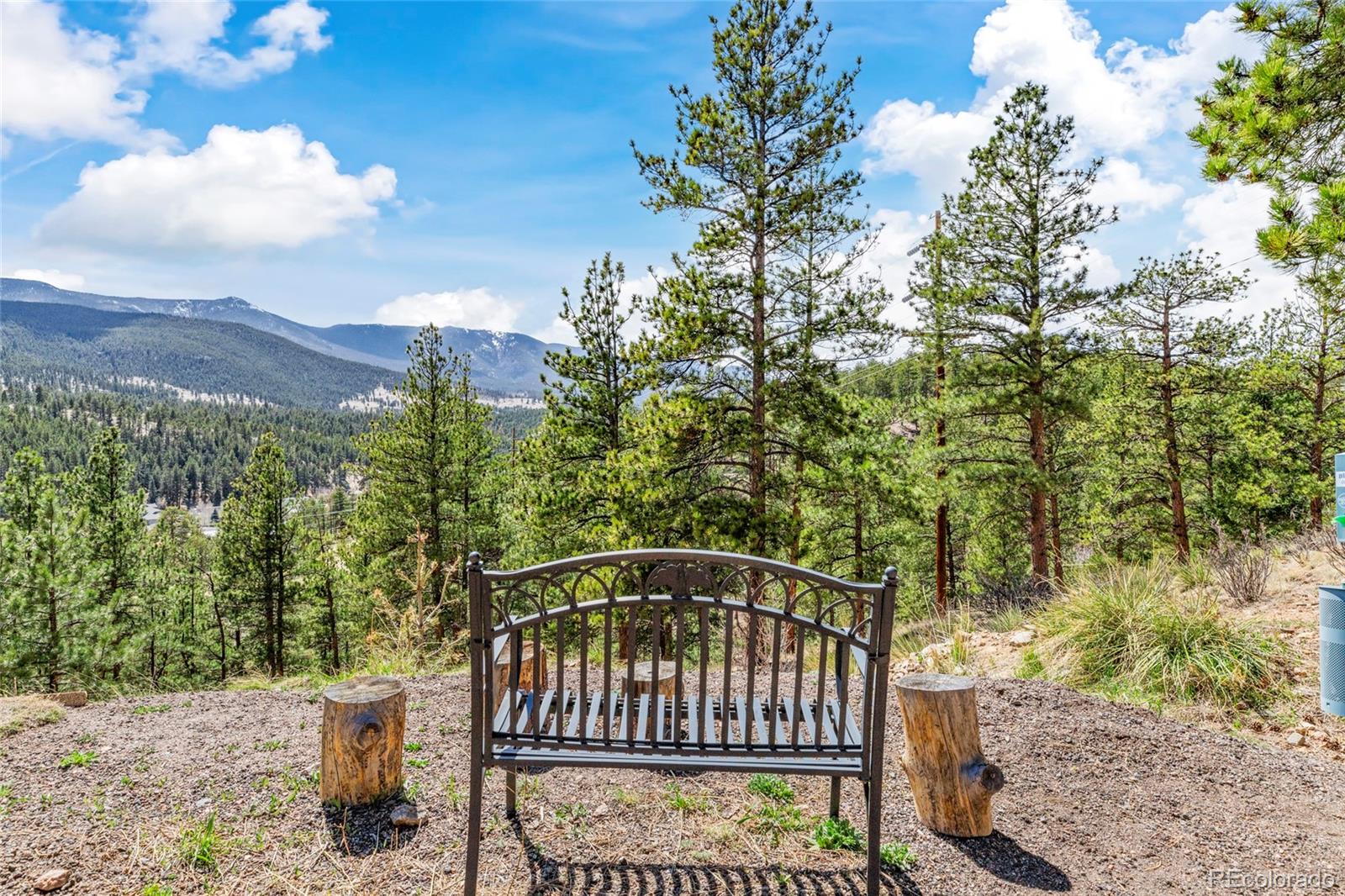 Mountain and forest views from a gravel seating area with a metal bench.