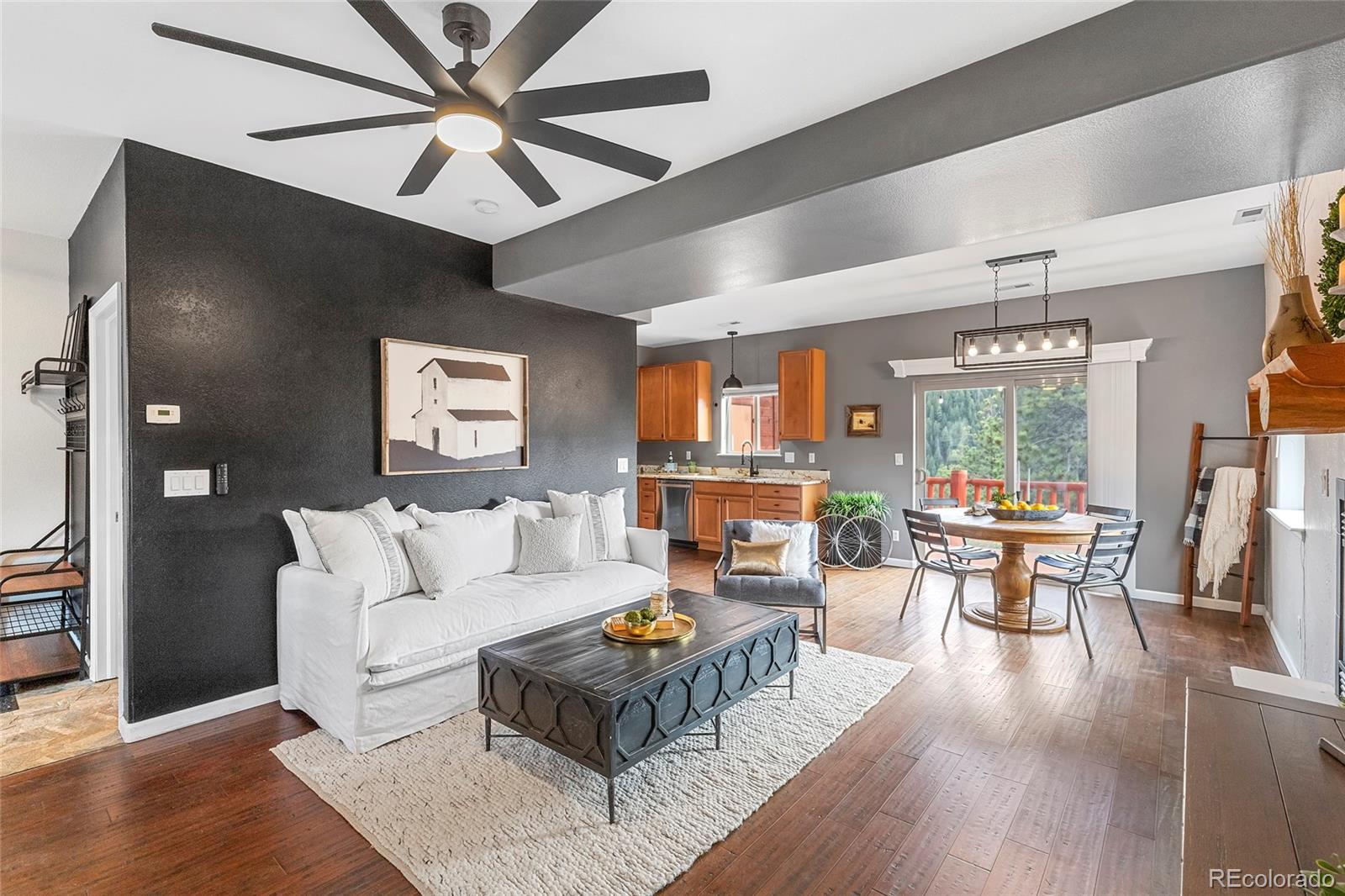 Open living room with white sofa, dark accent wall, and adjoining kitchen and dining area.
