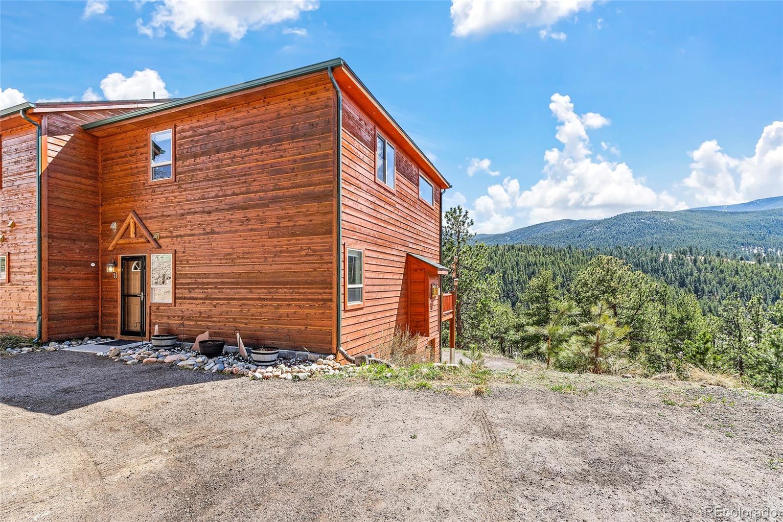 Wood-sided home with a gravel driveway, surrounded by forest and mountain views.