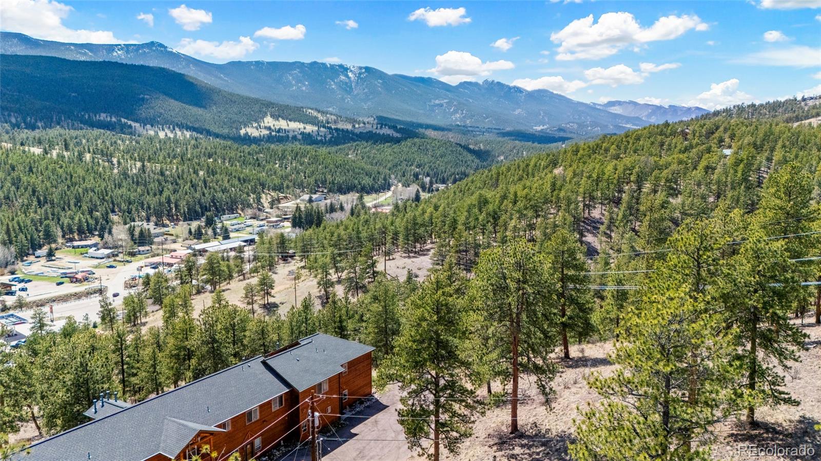 Aerial view of a mountain valley and pine-covered hills, with a residence in the foreground.