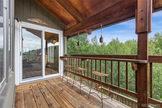 Covered wooden deck with bar stools overlooking trees.
