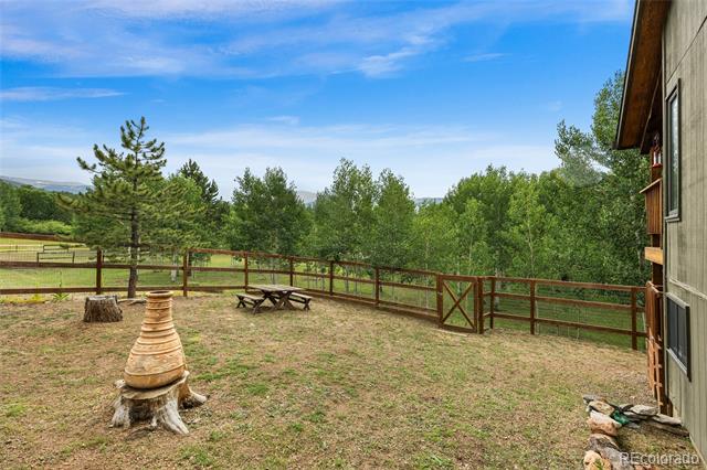 Fenced backyard with a picnic table and chiminea, surrounded by mature trees.