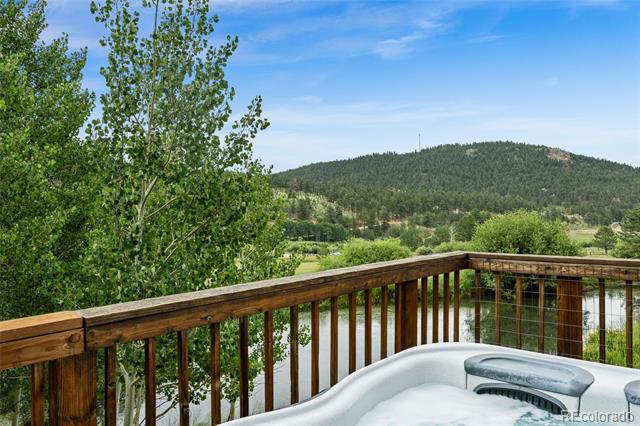 Deck hot tub overlooking a river and forested mountain, framed by leafy trees.