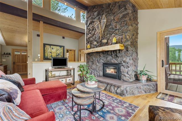 Living room with a tall stone fireplace, vaulted wood ceiling, and red sectional sofa.