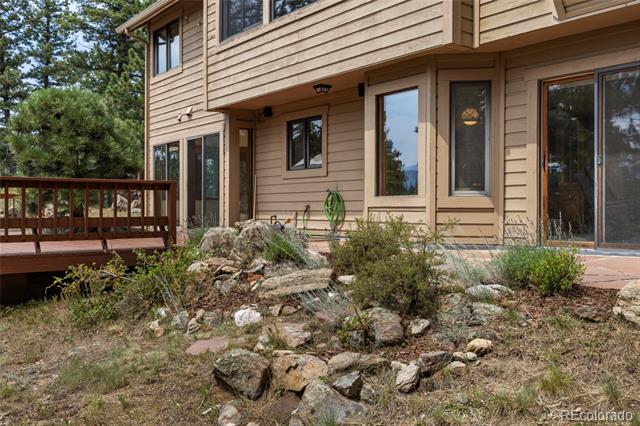 Tan-sided home with a wooden deck and rocky landscaping in the foreground.