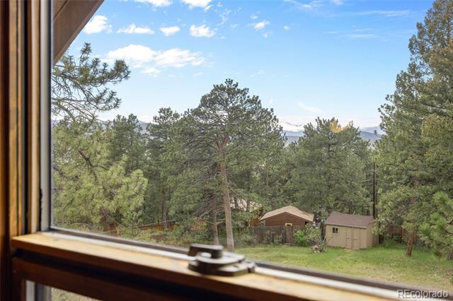 Wooded yard with two sheds and distant mountain ridges, viewed through a window.