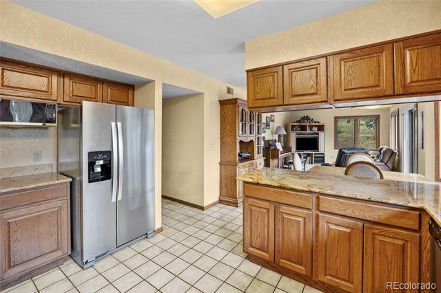 Kitchen with oak cabinetry, stainless steel refrigerator, and a granite-topped island opening to the living area.