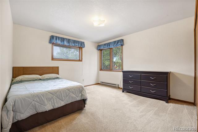 Bedroom with a bed, beige carpet, two curtained windows, and a dark dresser.