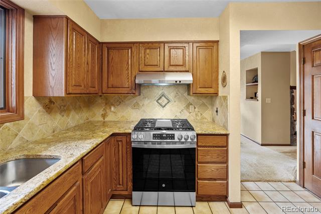 Kitchen with wood cabinets, granite counters, stainless steel range, and tile backsplash.