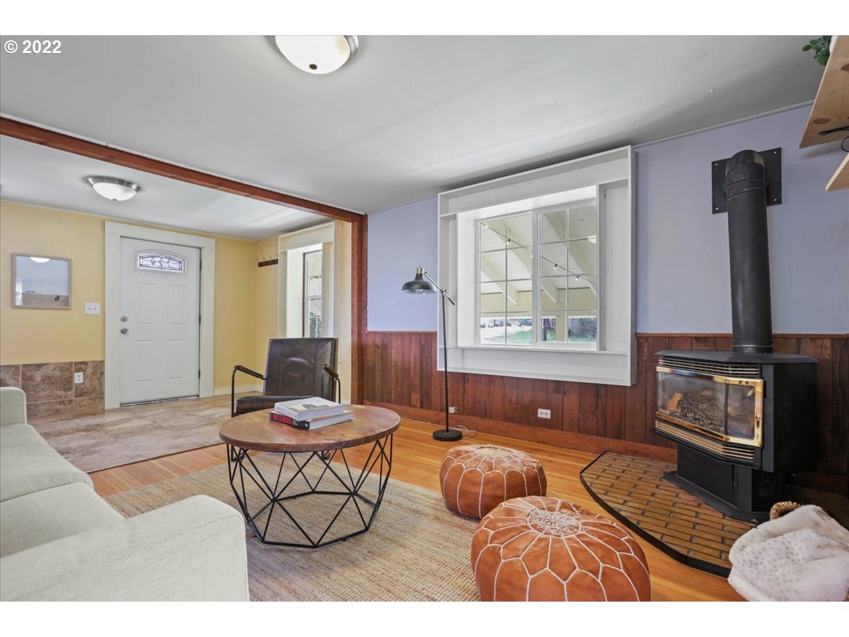 Living room with a black wood stove, wood paneling, and leather poufs.