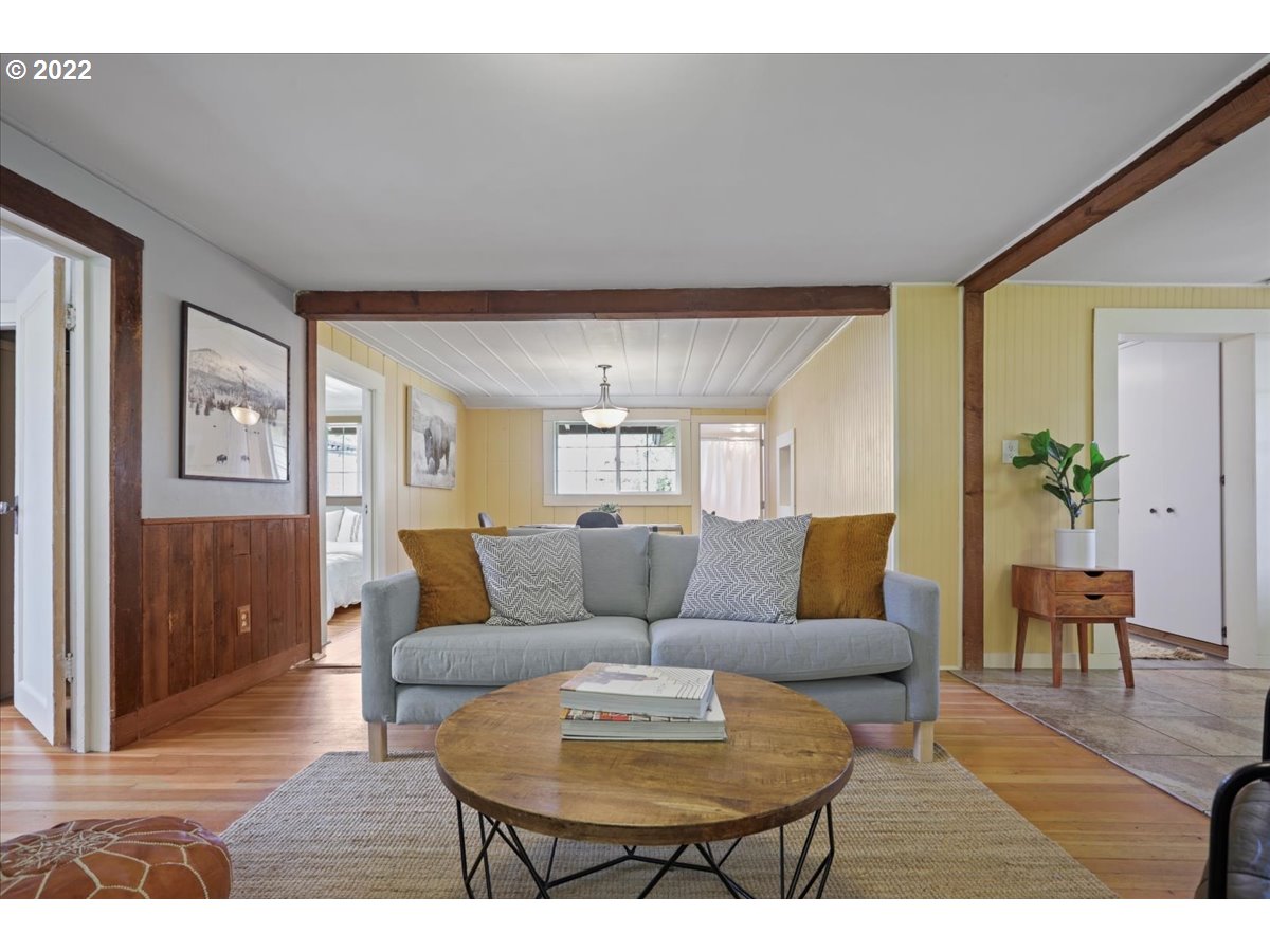 Living room with a gray sofa, round wooden coffee table, exposed beams, and yellow paneled walls.