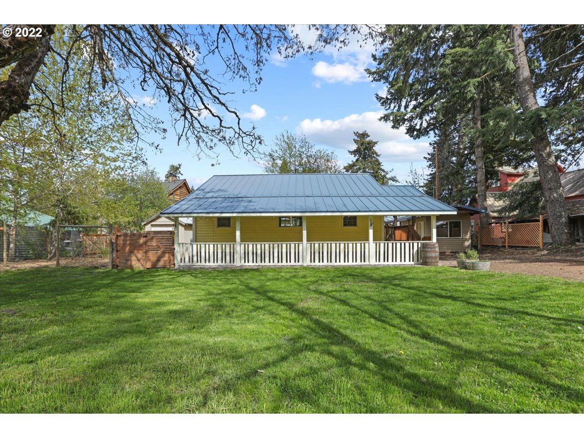Yellow-sided house with a broad metal roof and covered porch behind a green lawn.