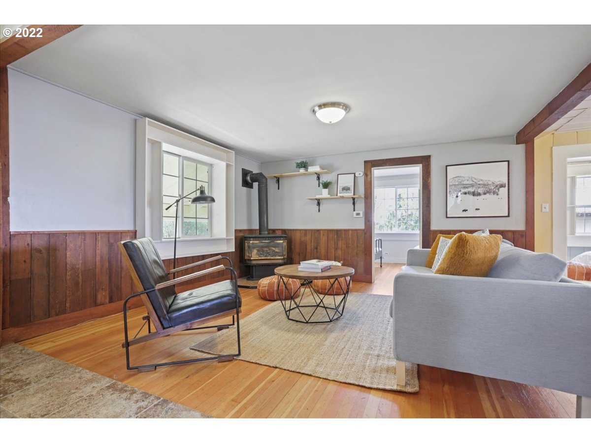 Living room with wood-paneled walls, hardwood floors, a wood-burning stove, and a gray sofa.