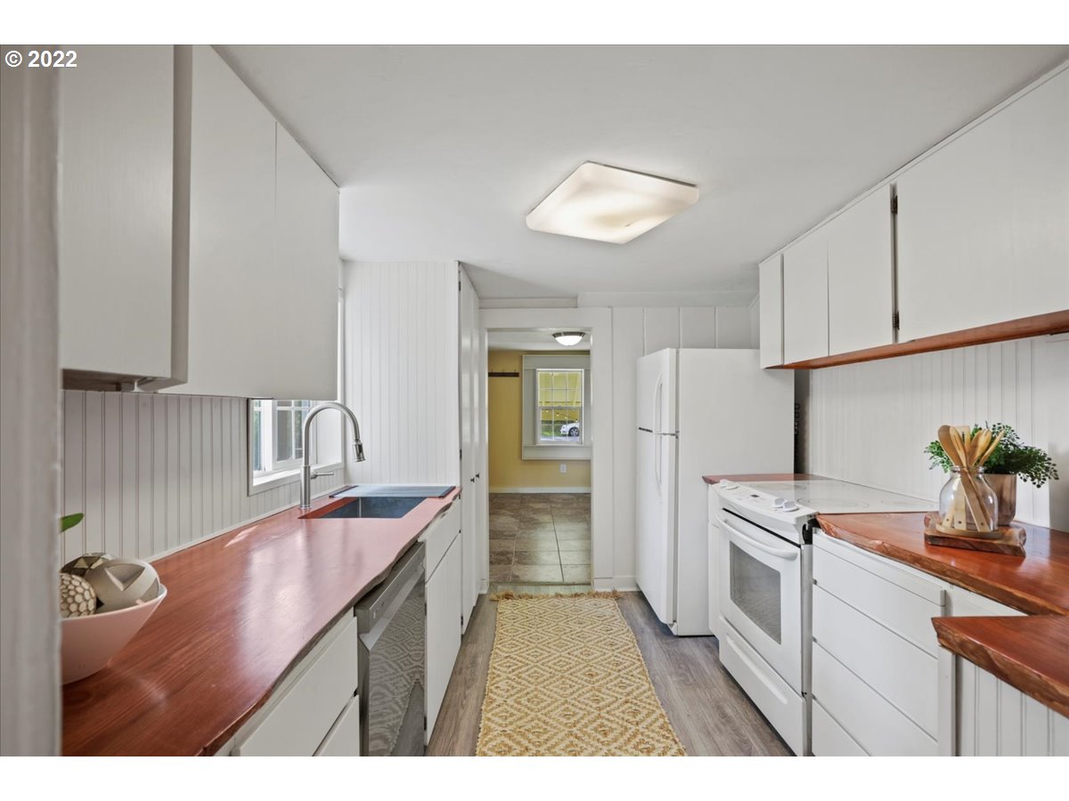 Galley kitchen with reddish wood countertops, white cabinets, and a patterned runner.