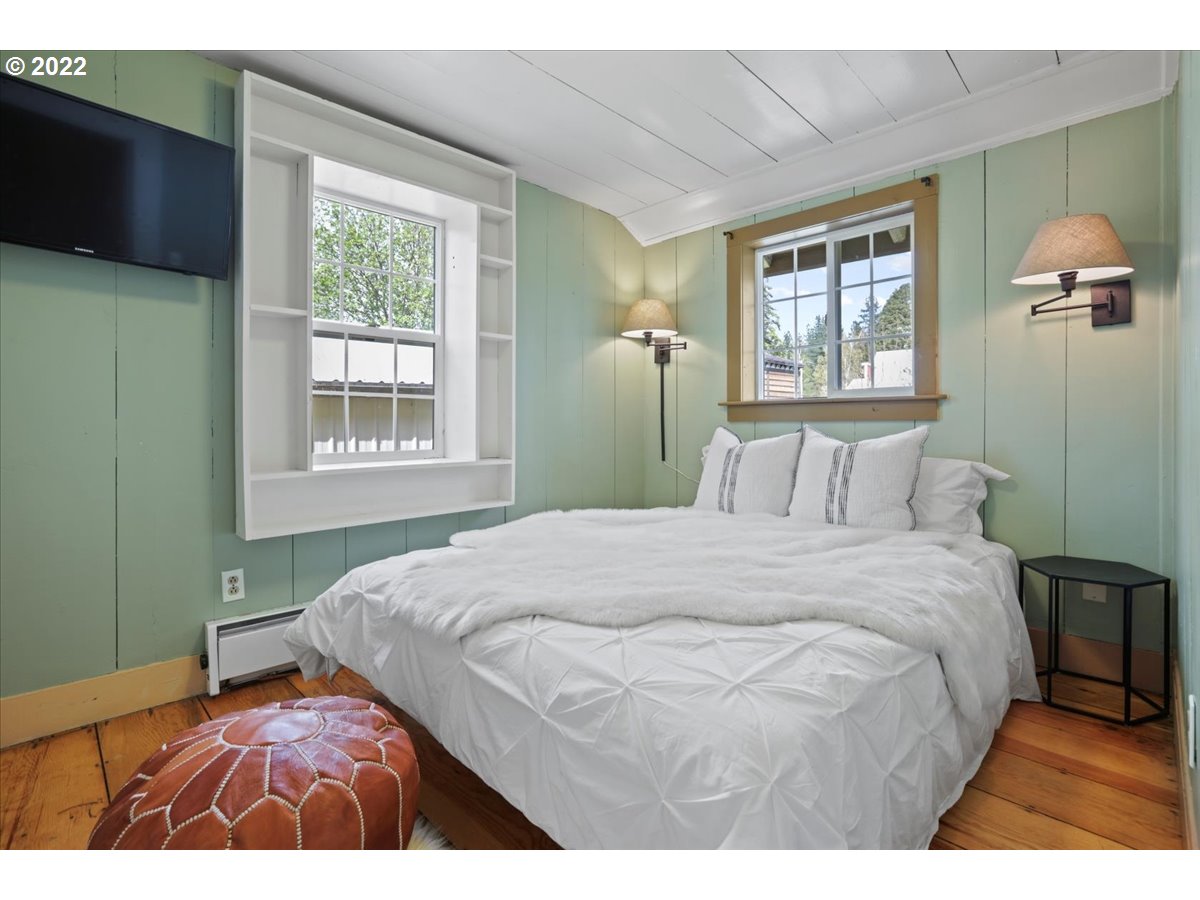 Bedroom with a white bed, green paneled walls, built-in window shelving, and warm wood floors.