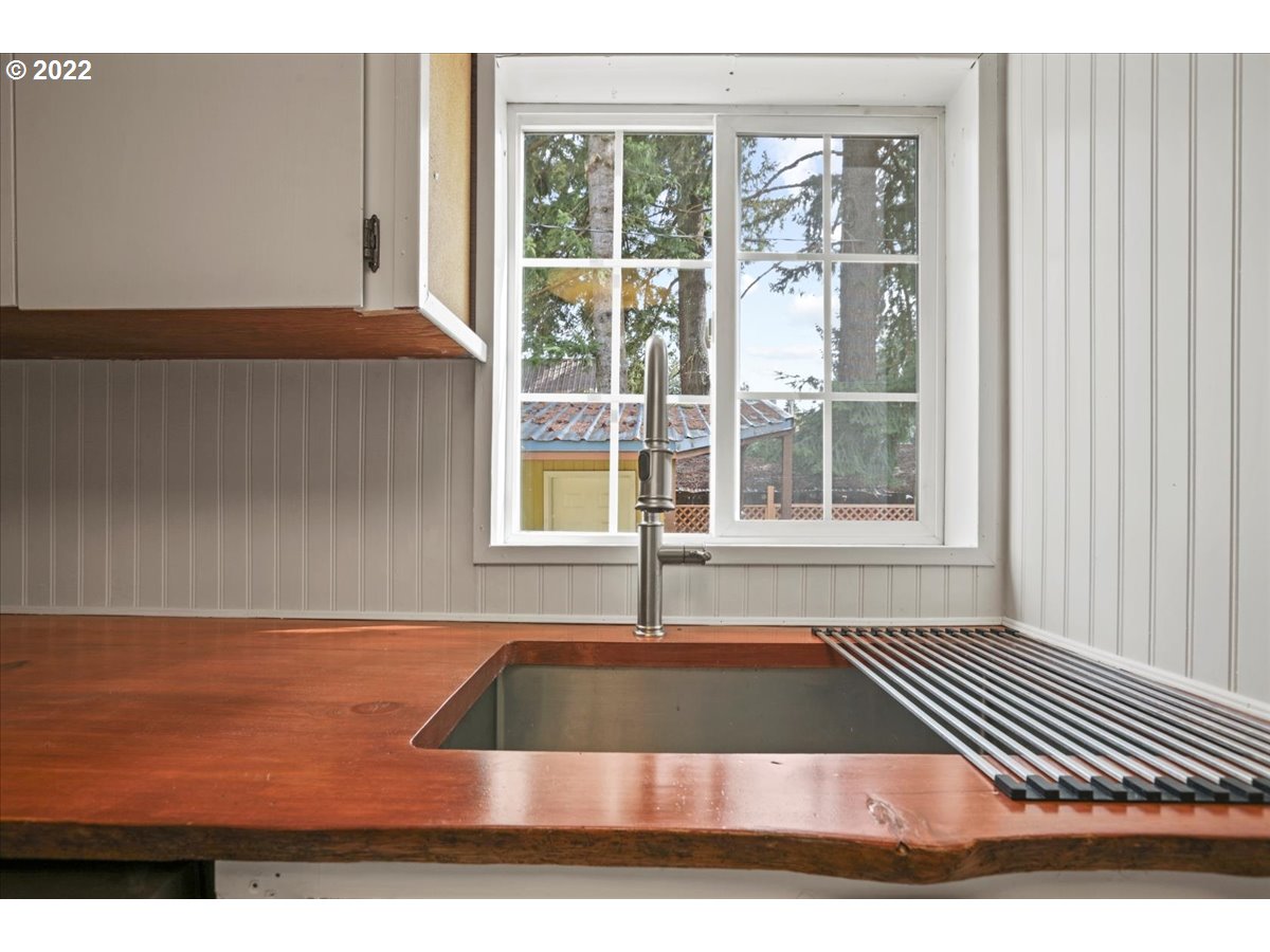 Kitchen sink in a warm wood countertop beneath a window, with a tall faucet and metal drainboard.