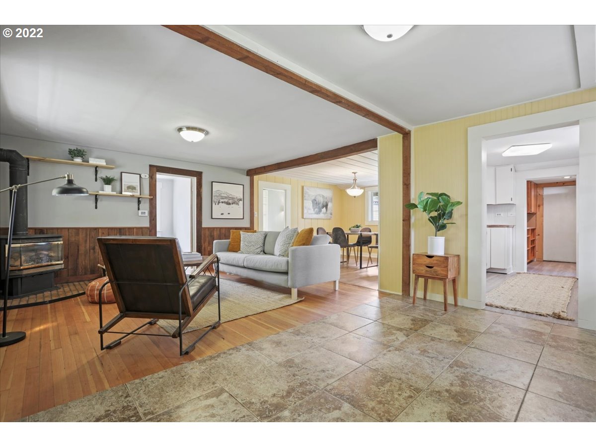 Living room with exposed wood beams, a wood-burning stove, and an open dining area.
