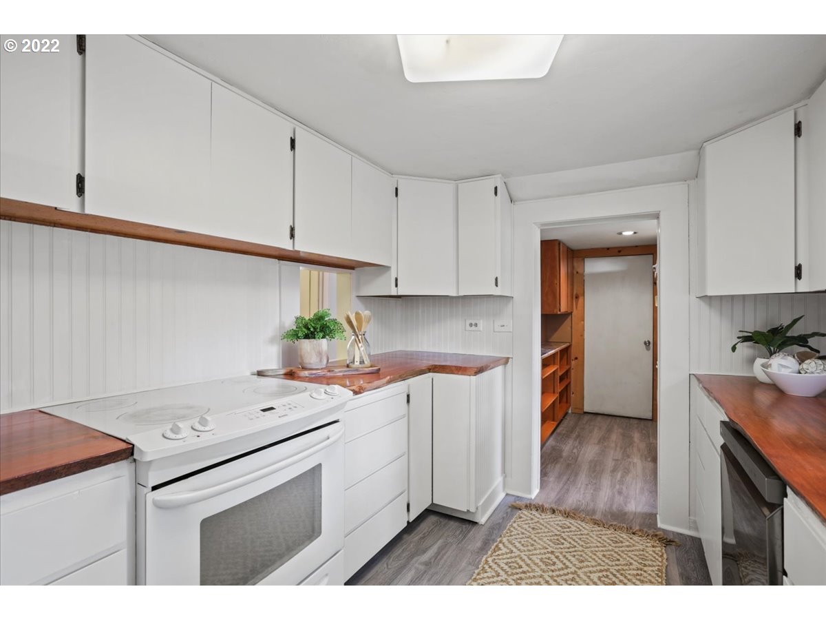 Kitchen with white cabinetry, reddish wood countertops, and a doorway leading to a hall with built-in shelves.