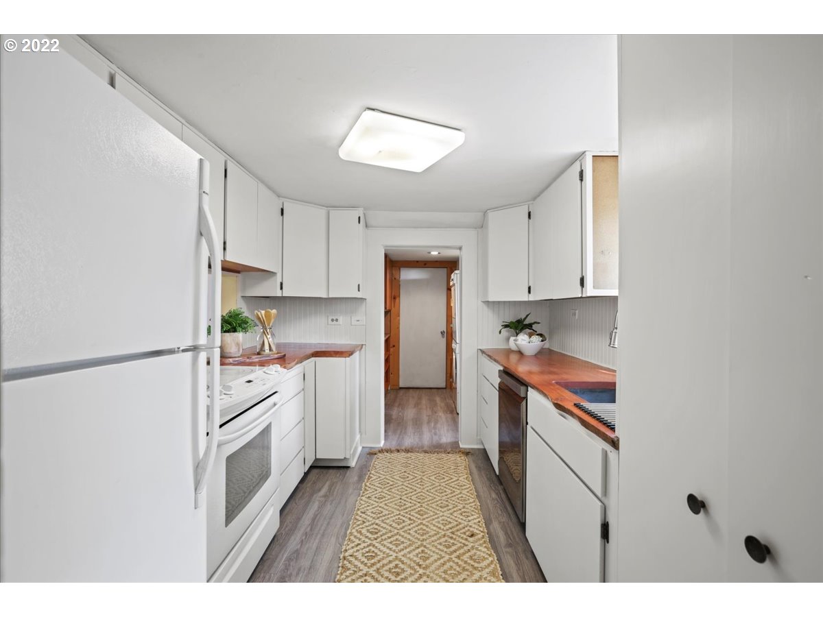 Galley kitchen with white cabinets, warm wood countertops, and a patterned runner.