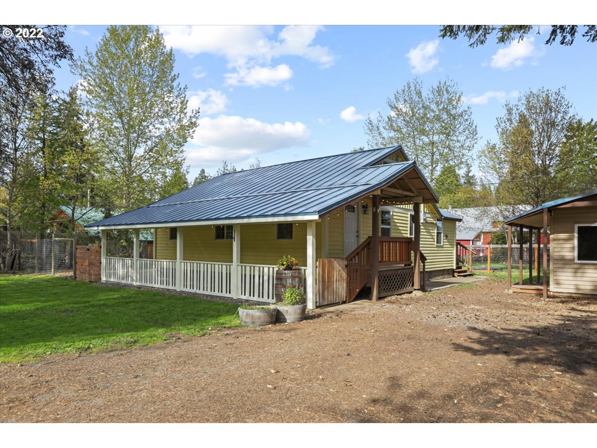 Olive-green home with a blue-gray metal roof, covered porch, and wooden entry steps.