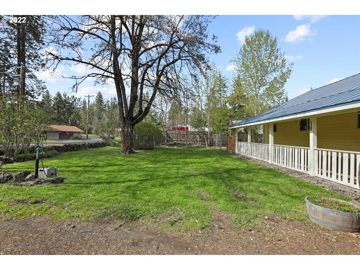 Grassy yard beside a yellow house with a covered porch and a large mature tree.