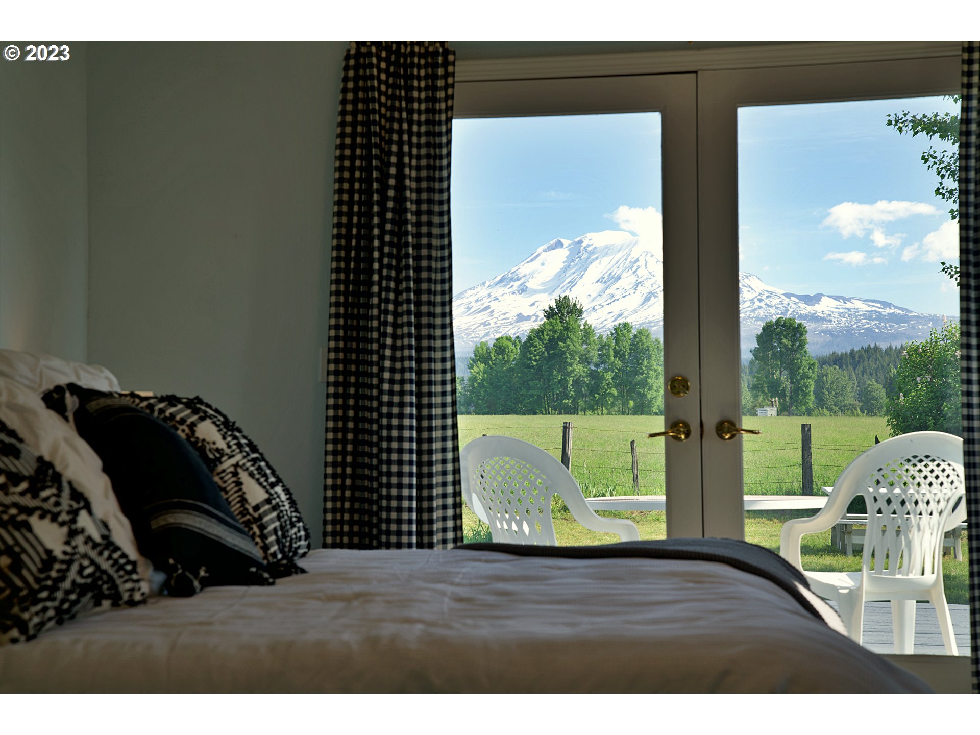 Bedroom with glass doors framing a view of snow-covered Mount Adams and a green lawn.